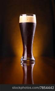 Tall glass of dark beer over a dark background lit yellow