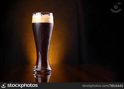 Tall glass of dark beer over a dark background lit yellow