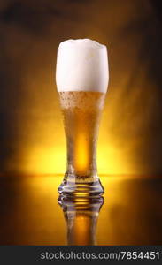 Tall glass of light beer with a rich foam over a yellow background