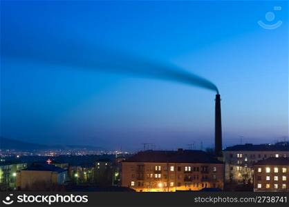 tall smokestack belches smoke into sky over night city, copy space