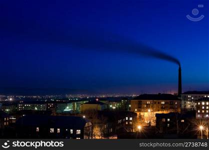 tall smokestack belches smoke into sky over night city, copy space