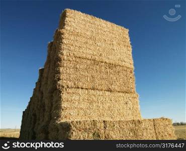 Tall stack of bales of hay in rural setting.