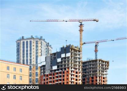 Tall tower cranes on the construction of a monolithic frame concrete structure of residential complexes against a cloudy blue sky. Copy space.. Construction of high rise residential complexes according to the modern method of monolithic frame technology.