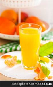 Tangerine orange juice in glass and fresh fruits with leaves on white wooden kitchen background closeup. Healthy and tasty refreshing summer beverage