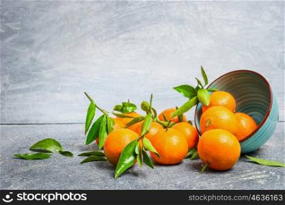 Tangerines with green leaves and bowl on rustic background, side view