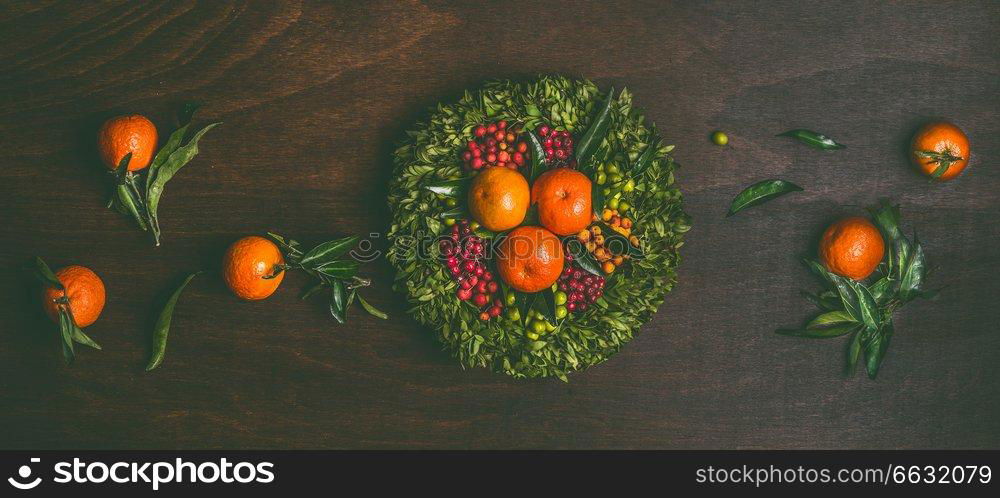 Tangerines with leaves wreath on dark rustic background, top view