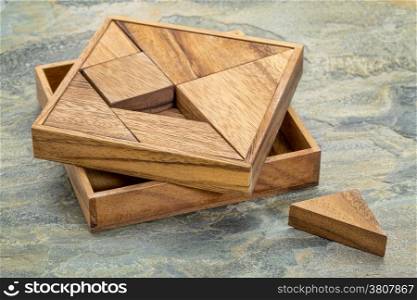 Tangram, a traditional Chinese Puzzle Game made of different wood parts to build abstract figures from them, slate rock background