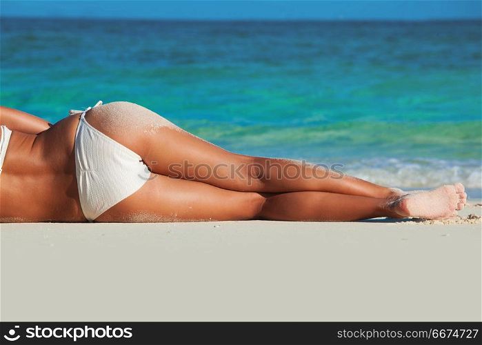 Tanned woman in bikini. Tanned woman body in red bikini laying in beach, blue sea water in background