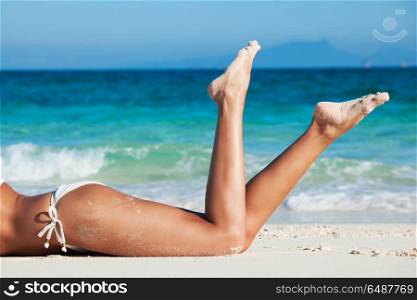 Tanned woman in bikini. Tanned woman in bikini laying in beach, view on legs, blue sea water in background