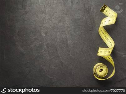 tape measure on slate stone background, top view