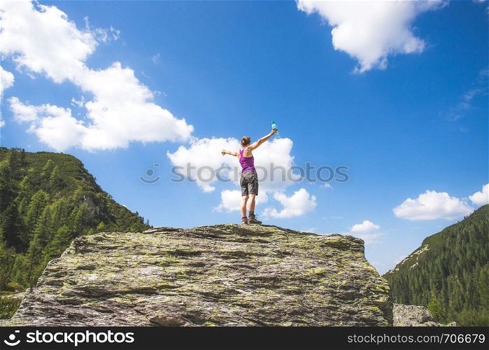 Target achieved: Sporty girl is standing on a big rock and raises her hands up in the air