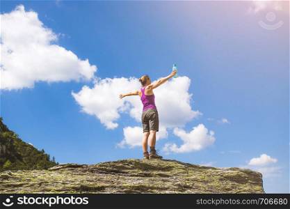 Target achieved: Sporty girl is standing on a big rock and raises her hands up in the air