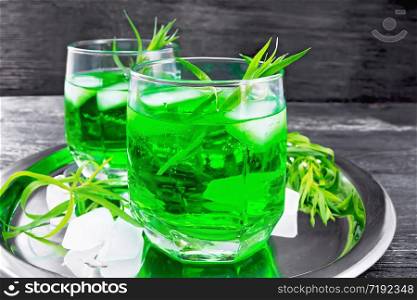 Tarkhun lemonade with ice in two glasses on a silver tray on wooden board background