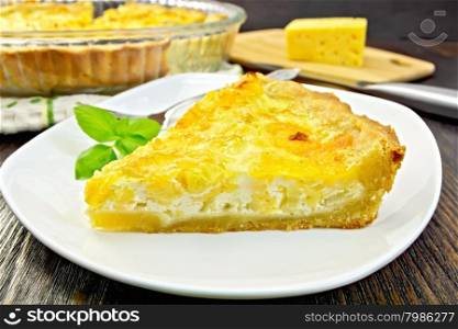 Tart with cheese, leek and sour cream and egg cream in a dish, cheese and knife on a wooden boards background