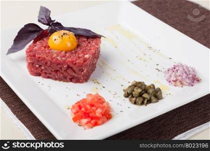 tartar of beef with egg yolk, pepper, capers and onions on a white plate