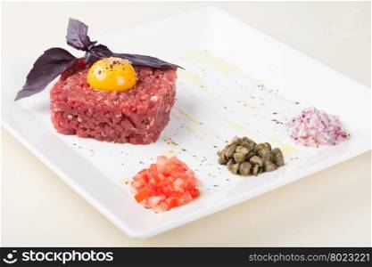tartar of beef with egg yolk, pepper, capers and onions on a white plate