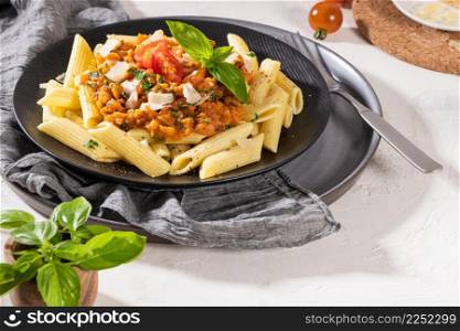 Tasty appetizing classic italian penne pasta with vegetarian lentil bolognese sauce, cheese parmesan and basil on plate on light table. Healthy eating concept.