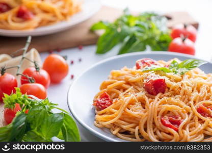 Tasty appetizing classic italian spaghetti pasta with tomato sauce, cheese parmesan and basil on plate and ingredients for cooking pasta on white marble table.