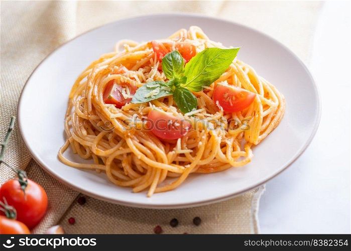Tasty appetizing classic italian spaghetti pasta with tomato sauce, cheese parmesan and basil on plate and ingredients for cooking pasta on white marble table.