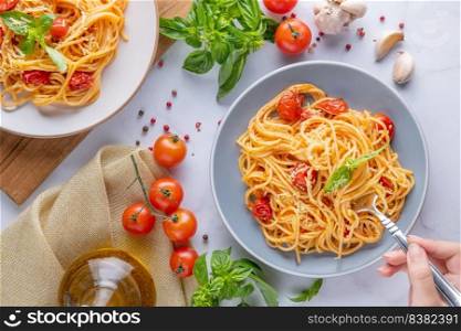 Tasty appetizing classic italian spaghetti pasta with tomato sauce, cheese parmesan and basil on plate and ingredients for cooking pasta on white marble table. Flat lay top view copy space.