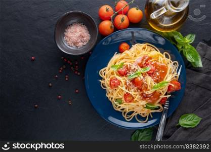 Tasty appetizing classic italian spaghetti pasta with tomato sauce, cheese parmesan and basil on plate  and ingredients for cooking pasta on dark table. Flat lay top view copy space.