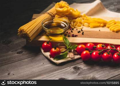 Tasty appetizing italian spaghetti pasta ingredients for kitchen cuisine with tomato, cheese parmesan, olive oil, fettuccine and basil on wooden brown table. Food Italian recipe homemade. Top view