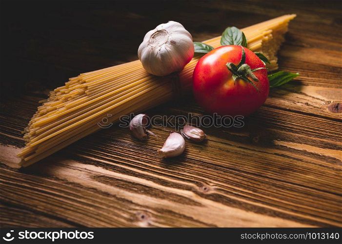 Tasty appetizing italian spaghetti pasta ingredients for kitchen cuisine with tomato, garlic and basil on wooden brown table. Food meal and Italian recipe homemade. Top view abgle above