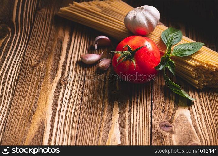 Tasty appetizing italian spaghetti pasta ingredients for kitchen cuisine with tomato, garlic and basil on wooden brown table. Food meal and Italian recipe homemade. Top view abgle above