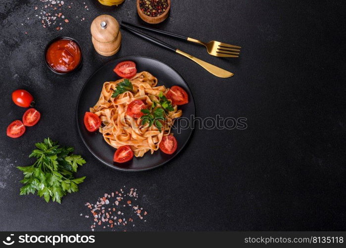 Tasty appetizing pasta tagliatelle spaghetti with tomato sauce and parmesan. Served on a black plate on a dark concrete table. Tasty appetizing pasta tagliatelle spaghetti with tomato sauce and parmesan