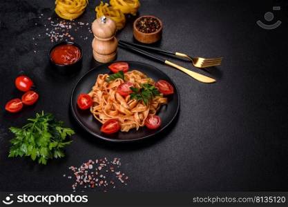 Tasty appetizing pasta tagliatelle spaghetti with tomato sauce and parmesan. Served on a black plate on a dark concrete table. Tasty appetizing pasta tagliatelle spaghetti with tomato sauce and parmesan