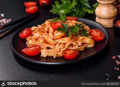 Tasty appetizing pasta tagliatelle spaghetti with tomato sauce and parmesan. Served on a black plate on a dark concrete table. Tasty appetizing pasta tagliatelle spaghetti with tomato sauce and parmesan