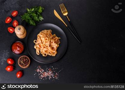 Tasty appetizing pasta tagliatelle spaghetti with tomato sauce and parmesan. Served on a black plate on a dark concrete table. Tasty appetizing pasta tagliatelle spaghetti with tomato sauce and parmesan