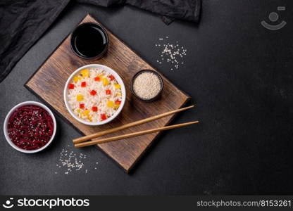 Tasty Asian dish of rice, pepper, spices and herbs in a black plate on a dark concrete background. Tasty Asian dish of rice, pepper, spices and herbs
