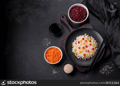 Tasty Asian dish of rice, pepper, spices and herbs in a black plate on a dark concrete background. Tasty Asian dish of rice, pepper, spices and herbs