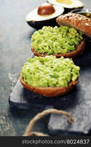 Tasty avocado sandwiches on slate background