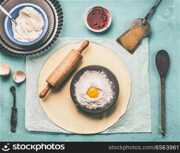 Tasty baking. Dough, rolling pin and bowl with flour and egg on light blue kitchen table background, top view
