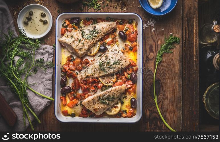 Tasty Bass fish fillets in Mediterranean sauce with tomatoes, olives and capers in baking pan on rustic wooden background with ingredients. Top view