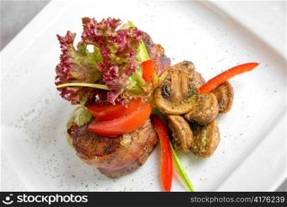 Tasty beef steak grilled in a cast-iron ribbed fry pan with bacon decorated with vegetables and roasted mushrooms