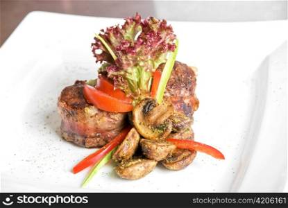 Tasty beef steak grilled in a cast-iron ribbed fry pan with bacon decorated with vegetables and roasted mushrooms
