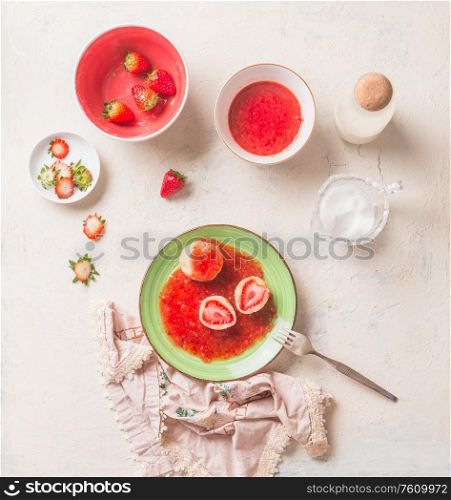 Tasty boiled cottage dumplings stuffed with fresh strawberries with sweet berries sauce in green plate on white kitchen table. Top view. Summer sweet food. Home cooking. Seasonal meal. Knedliki .