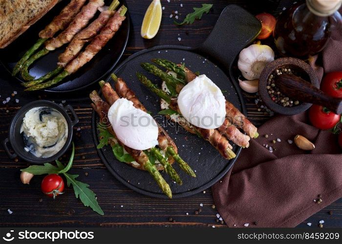 Tasty breakfast - toasts with cream cheese, poached eggs and Asparagus wrapped with bacon and spices on a plate.. Tasty breakfast - toasts with cream cheese, poached eggs and Asparagus wrapped with bacon and spices on a plate