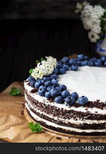 Tasty cake closeup with copy space. Homemade bird cherry cake with sour cream, decorated with blueberries and mint leaves on baking paper. Siberian traditional cake. Branch of flowering bird cherry.. Homemade bird cherry cake with sour cream, decorated with blueberries and mint leaves on baking paper. Close up