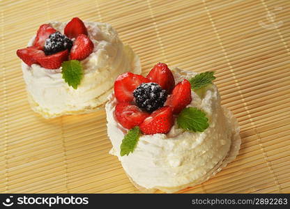 tasty cakes with white icing and strawberries on bamboo table cloth