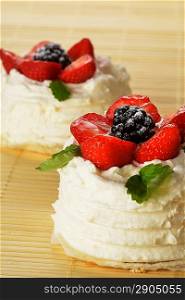 tasty cakes with white icing and strawberries on bamboo table cloth