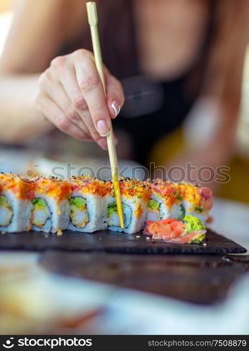 Tasty california roll, a woman using chopsticks eats delicious healthy sushi, enjoying oriental food, having lunch in luxury sushi restaurant