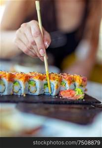 Tasty california roll, a woman using chopsticks eats delicious healthy sushi, enjoying oriental food, having lunch in luxury sushi restaurant