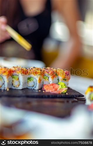 Tasty california roll, woman using chopsticks, eats delicious healthy sushi, enjoying oriental food, having lunch in a sushi bar, an asian restaurant menu