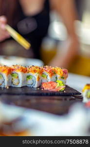 Tasty california roll, woman using chopsticks, eats delicious healthy sushi, enjoying oriental food, having lunch in a sushi bar, an asian restaurant menu