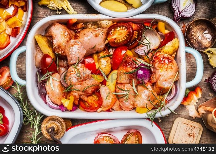 Tasty chicken with colorful vegetables and red sweet paprika in casserole, preparation on rustic wooden background with bowls and cutting cooking ingredients, top view, close up