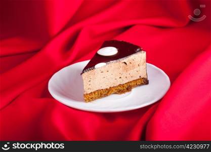 tasty chocolate cake on the plate on red silk background. Shallow focus